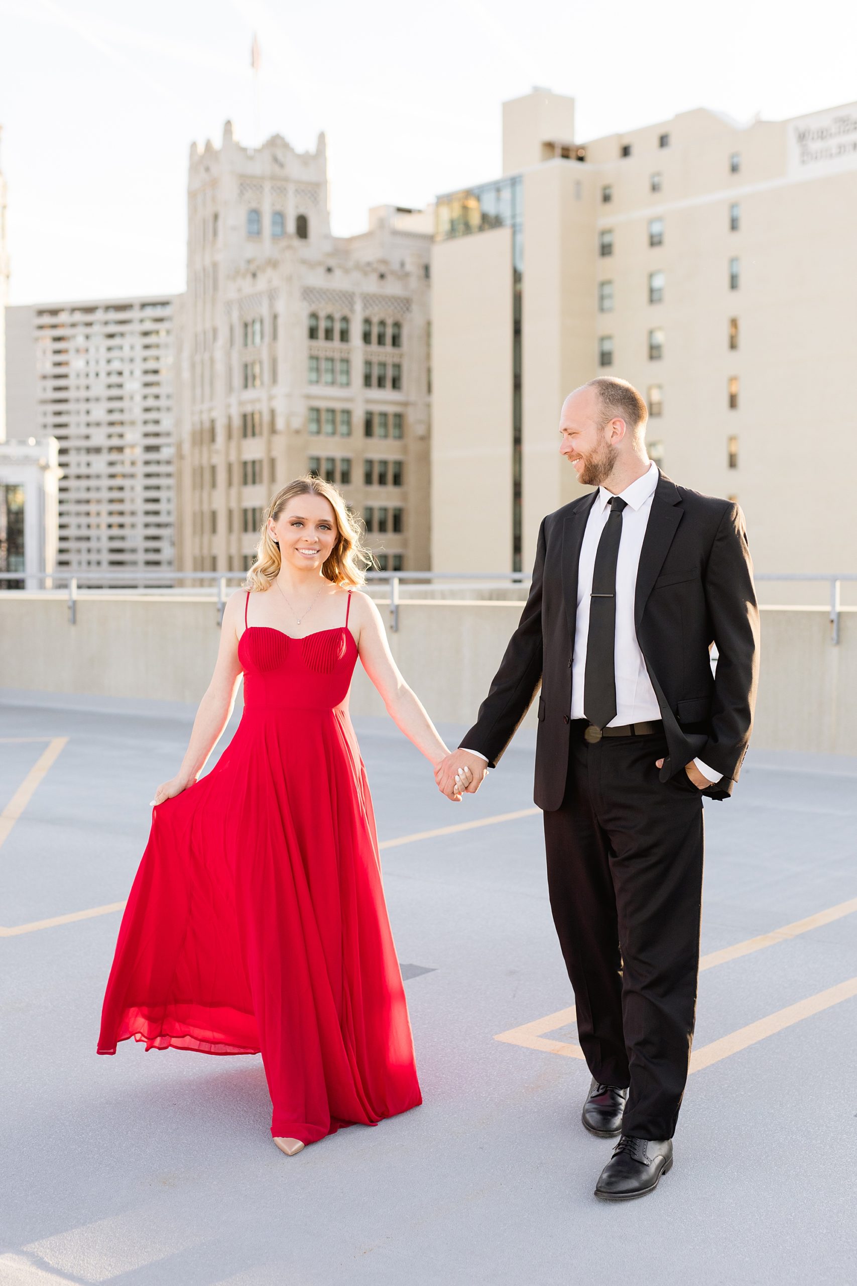 woman in a red dress with man in a black suit posing for engagement photos